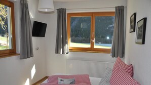 A bedroom with a bed, checkered bedding, a window with curtains, a radiator, and a TV on the wall. - Chalet in Steeg Near Ski Slopes (Steeg)