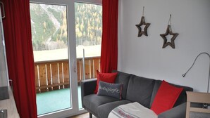 A living room with a grey sofa, red and white cushions, a blanket, and two star decorations on the wall. - Chalet in Steeg Near Ski Slopes (Steeg)