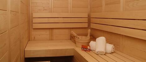 Uma sauna de madeira com bancos, um banquinho, um balde e toalhas.