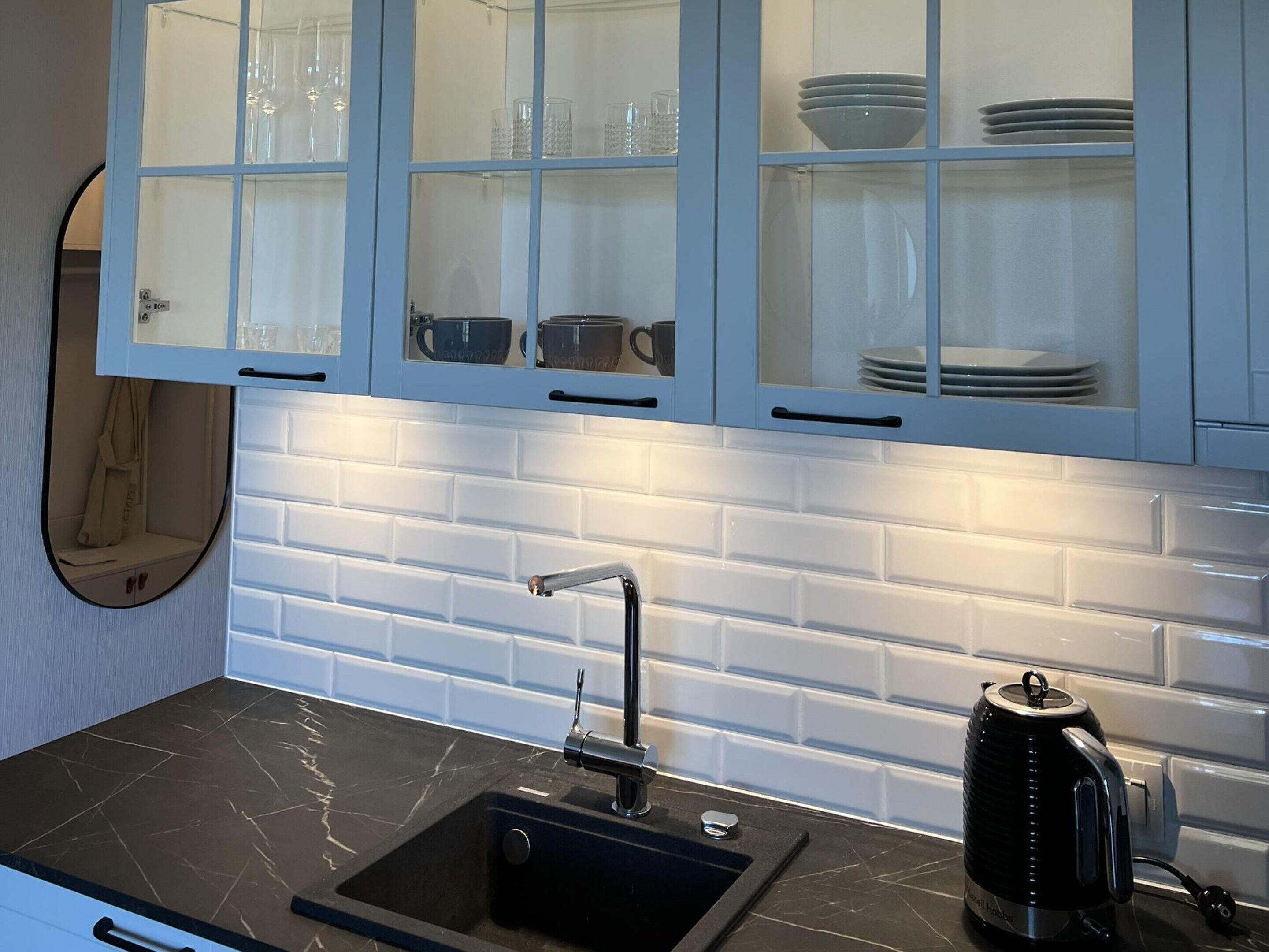 Een moderne keuken met witte metrotegels, een zwarte spoelbak en een waterkoker.
