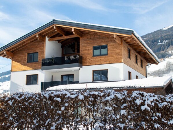 A two-story wooden house with a balcony, surrounded by snow-covered hills. - Apartment in Bramberg Near Cable Car (Bramberg am Wildkogel)