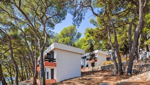 A modern building with a flat roof, surrounded by trees and a rocky landscape. - Jelsa Resort Apartment With Pool (Jelsa)