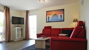Un salón con un sofá rojo, una mesa de centro, un televisor sobre un mueble bajo y un cuadro de un muelle en la pared.