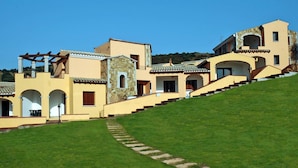 A multi-story building with a stone facade, multiple balconies, and a sloped roof. - Apartment in the Li Troni Residence in Budoni (Budoni)