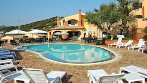 A pool area with lounge chairs and umbrellas, surrounded by buildings with a Mediterranean architectural style. - Apartment in the Li Troni Residence in Budoni (Budoni)