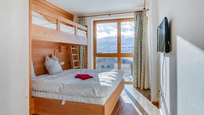 Une chambre avec un lit superposé, une fenêtre donnant sur une montagne et un téléviseur fixé au mur.