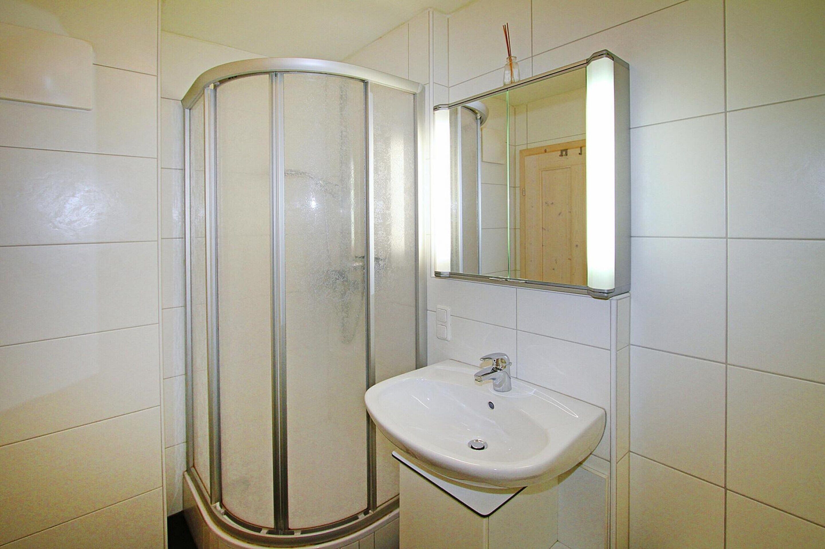 Ein Badezimmer mit Duschkabine, weißem Waschbecken und Spiegel darüber.