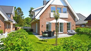 A two-story house with a brick exterior, a covered patio with a table and chairs, and a small garden area. - Ferienwohnung in Wyk auf Foehr (Wyk auf Foehr)