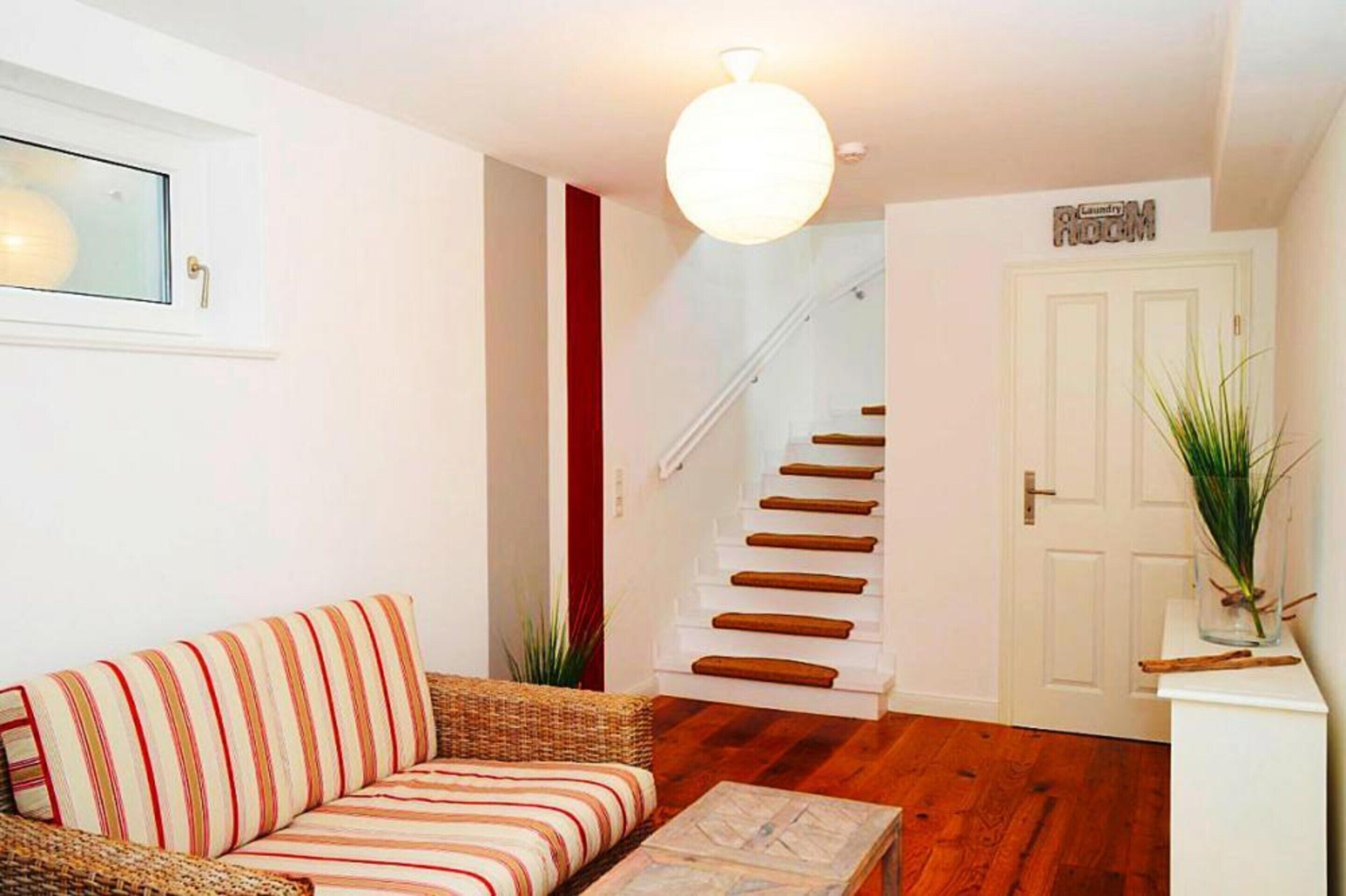 Un salon avec un canapé, un escalier, une porte portant l’inscription « buanderie » et une plante en pot.