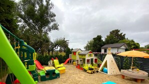 Une aire de jeux avec un toboggan, des balançoires et une petite structure en forme de maison.
