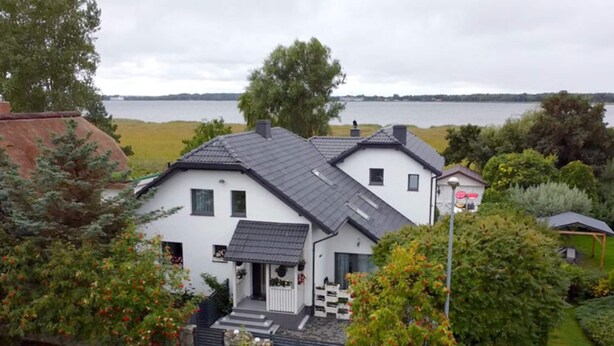 A two-story house with a sloped roof, a front porch, and a view of a lake. - Luxury Residence at the sea wth the Private Pool (Dziwnów)