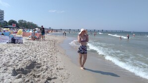 A beach with people walking along the shore, umbrellas, and a pier in the background. - Luxury Residence at the sea wth the Private Pool (Dziwnów)