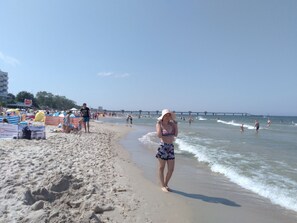 Une plage où l’on voit des gens se promener le long du rivage, des parasols et une jetée en arrière-plan.