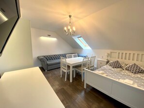Cozy loft-style apartment with a dining area, sofa, and bed, featuring a chandelier and skylight.