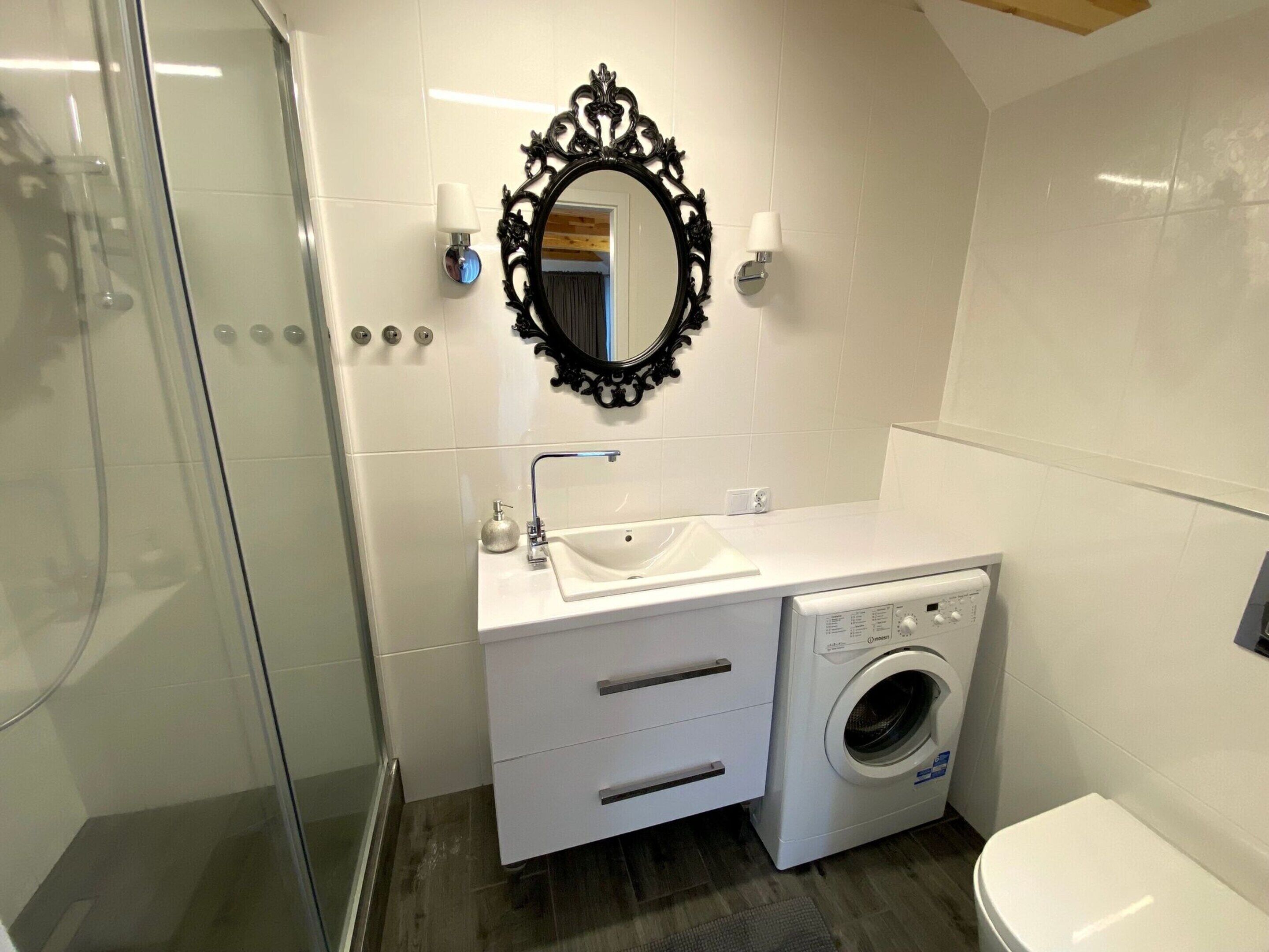 Une salle de bain avec une douche à parois de verre, un lavabo blanc avec un miroir au-dessus, et un lave-linge à chargement frontal.