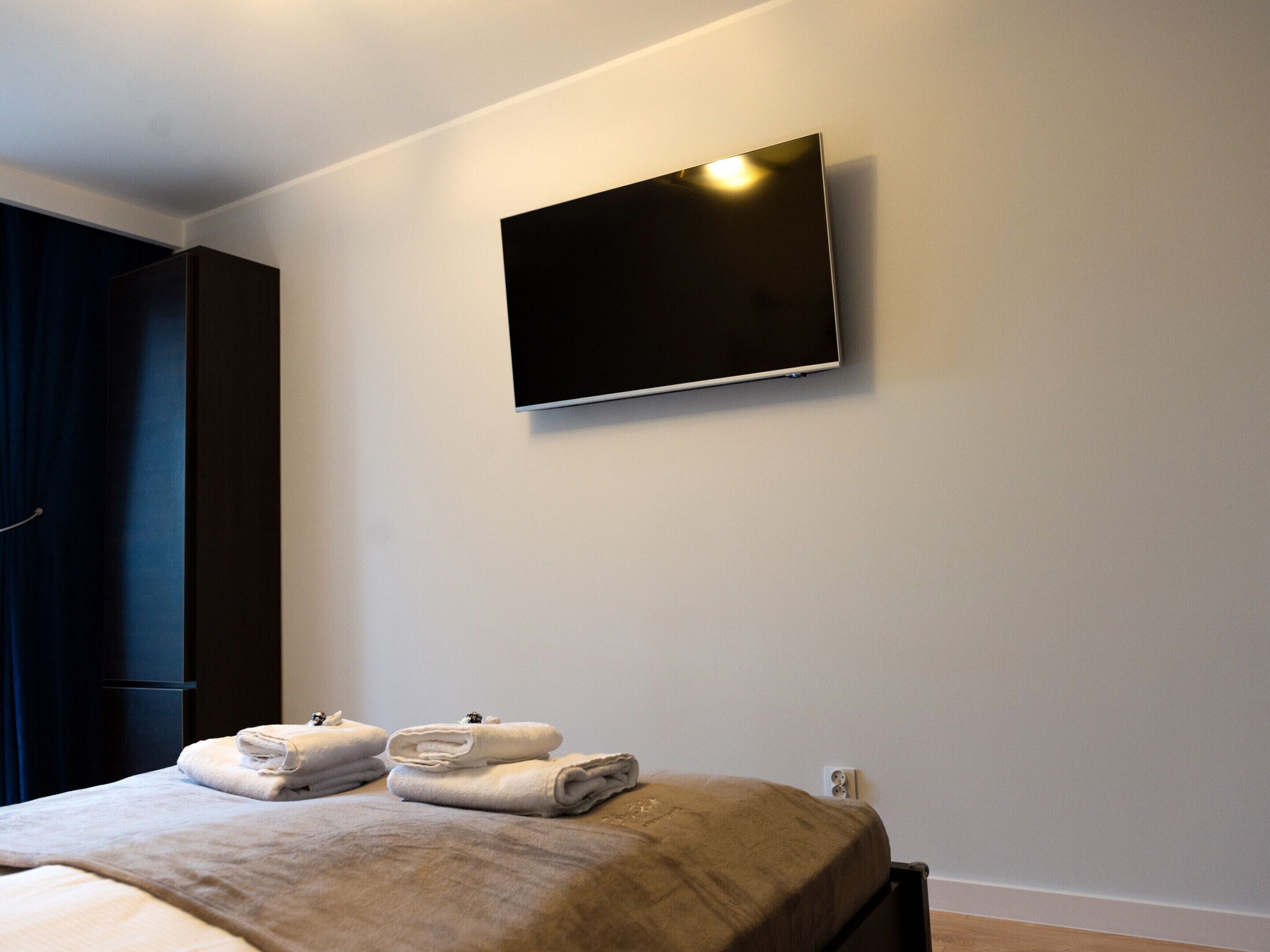 A hotel room with a bed, a flat-screen TV mounted on the wall, and a set of folded towels on the bed.