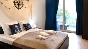 Camera d'albergo con un letto, un'ampia finestra con tende e un elemento decorativo a parete con una bussola, oltre a vista su del verde all'esterno.