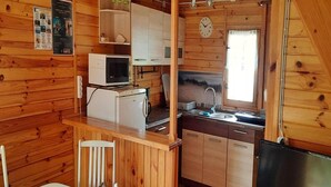 A cabin interior with a kitchen area, wooden walls, a dining table with chairs, a television, and a clock. - Comfortable House With Private Garden, Rusinowo (Postomino)