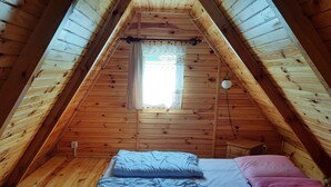 A small, wooden attic bedroom with a sloped ceiling, a window with lace curtains, and a bed with blue and pink bedding. - Comfortable House With Private Garden, Rusinowo (Postomino)