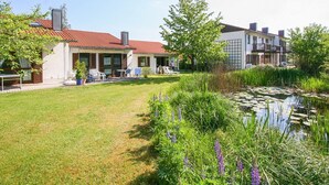 A residential building with a covered patio, a small pond, and surrounding greenery. - Ferienhaus in Falkenstein (Falkenstein)