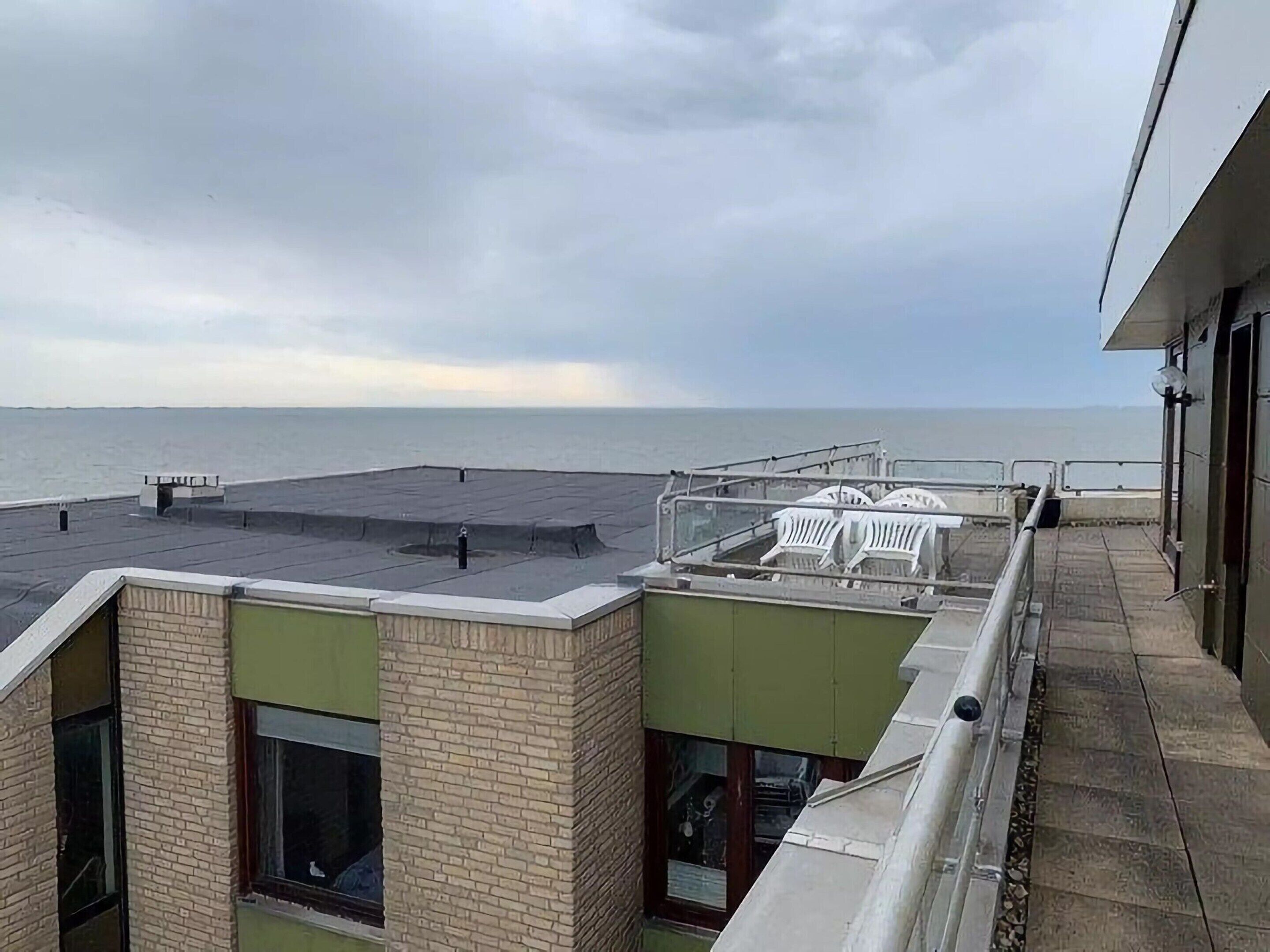 Terraza en la azotea con vistas al mar, que cuenta con una zona de estar con sillas blancas y una mesa pequeña.