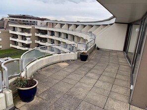 A balcony with a curved railing, potted plants, and a view of a multi-story building. - Ferienwohnung in Wyk auf Ftshr for 4 Personen (Wyk auf Foehr)