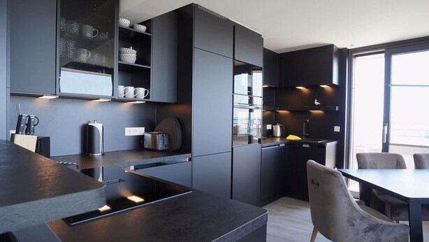 A modern kitchen with dark cabinetry, a central island, and a dining area with chairs. - Ferienwohnung in Wyk auf Ftshr for 4 Personen (Wyk auf Foehr)