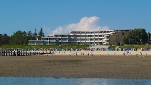 A beach with a large building in the background, a pier extending into the water, and people enjoying the beach. - Ferienwohnung in Wyk auf Ftshr for 4 Personen (Wyk auf Foehr)