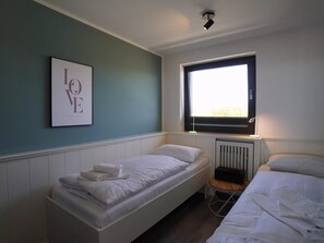 A bedroom with two beds, a radiator, a window, and a framed picture on the wall. - Ferienwohnung in Wyk auf Ftshr for 4 Personen (Wyk auf Foehr)