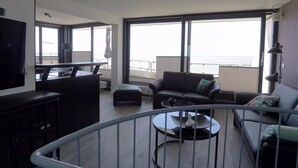 A modern living room with a large window, a round coffee table, a sofa, and a TV. - Ferienwohnung in Wyk auf Ftshr for 4 Personen (Wyk auf Foehr)