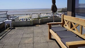 A terrace with a wooden bench and a small table, overlooking a beach. - Ferienwohnung in Wyk auf Ftshr for 4 Personen (Wyk auf Foehr)