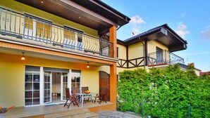 Une maison à deux étages avec un balcon, une terrasse dotée de mobilier d’extérieur et un jardin.