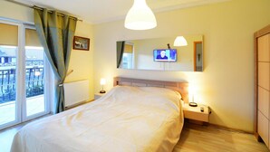 Une chambre à coucher avec un grand lit, des lampes de chevet, un téléviseur fixé au mur et une fenêtre avec des rideaux.