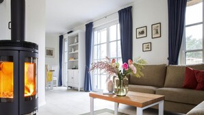 Un soggiorno moderno con un camino a legna nero, un tavolino in legno, un divano beige e un'ampia finestra con tende blu.