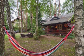 A wooden cabin with a porch, surrounded by tall trees and a hammock.