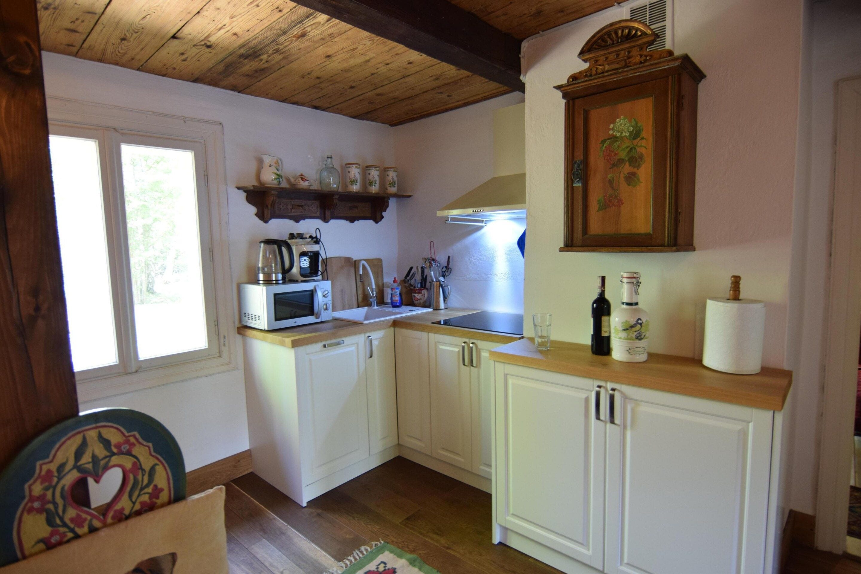 Una cocina con armarios blancos, microondas, tetera y techo de madera.