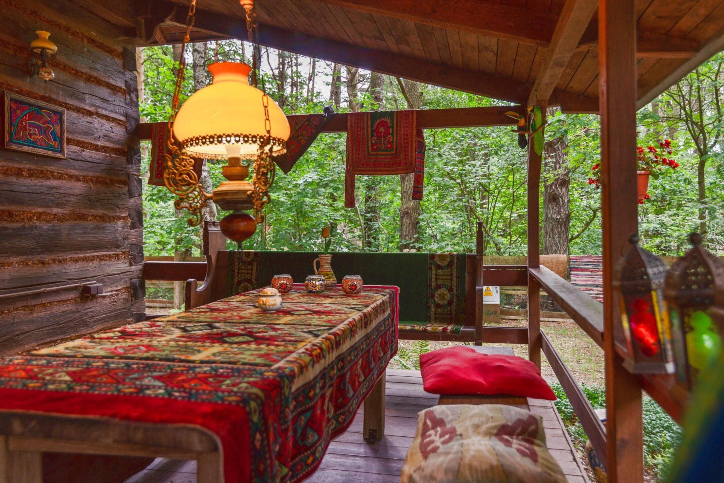 A wooden cabin with a bed, a hanging lamp, and a view of the forest.