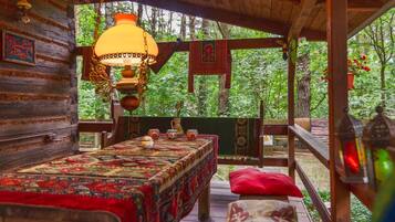A wooden cabin with a bed, a hanging lamp, and a view of the forest.