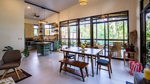 A spacious living area with a large dining table, comfortable seating, and a view of the outdoors through large windows. - Casa Aluem in the Forest Close to the Beach (Bahía Ballena)