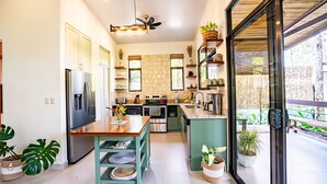 A modern kitchen with a central island, stainless steel appliances, and a large window overlooking a garden. - Casa Aluem in the Forest Close to the Beach (Bahía Ballena)