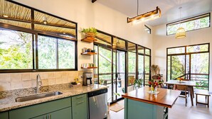 A modern kitchen with a large island, built-in appliances, and large windows offering views of greenery. - Casa Aluem in the Forest Close to the Beach (Bahía Ballena)