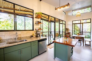 Een moderne keuken met een groot schiereiland, inbouwapparatuur en grote ramen met uitzicht op groen.