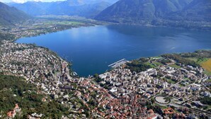 An aerial view of a coastal city with a large body of water, dense urban area, and mountainous backdrop. - Room-double Room With Air Conditioning - (Minusio)