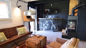 Una sala de estar acogedora con un sofá de cuero marrón, una mesa de centro de madera y un tapete estampado. Se observa una bicicleta dentro de una jaula de metal adosada a la pared, y una chimenea negra con chimenea.