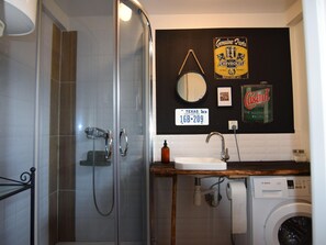 Ein Badezimmer mit Duschkabine, einem Waschbecken mit Holzplatte, einer Bosch Waschmaschine und einem Spiegel.