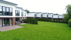 Un edificio residenziale moderno con un prato curato e una fila di alberi sempreverdi.