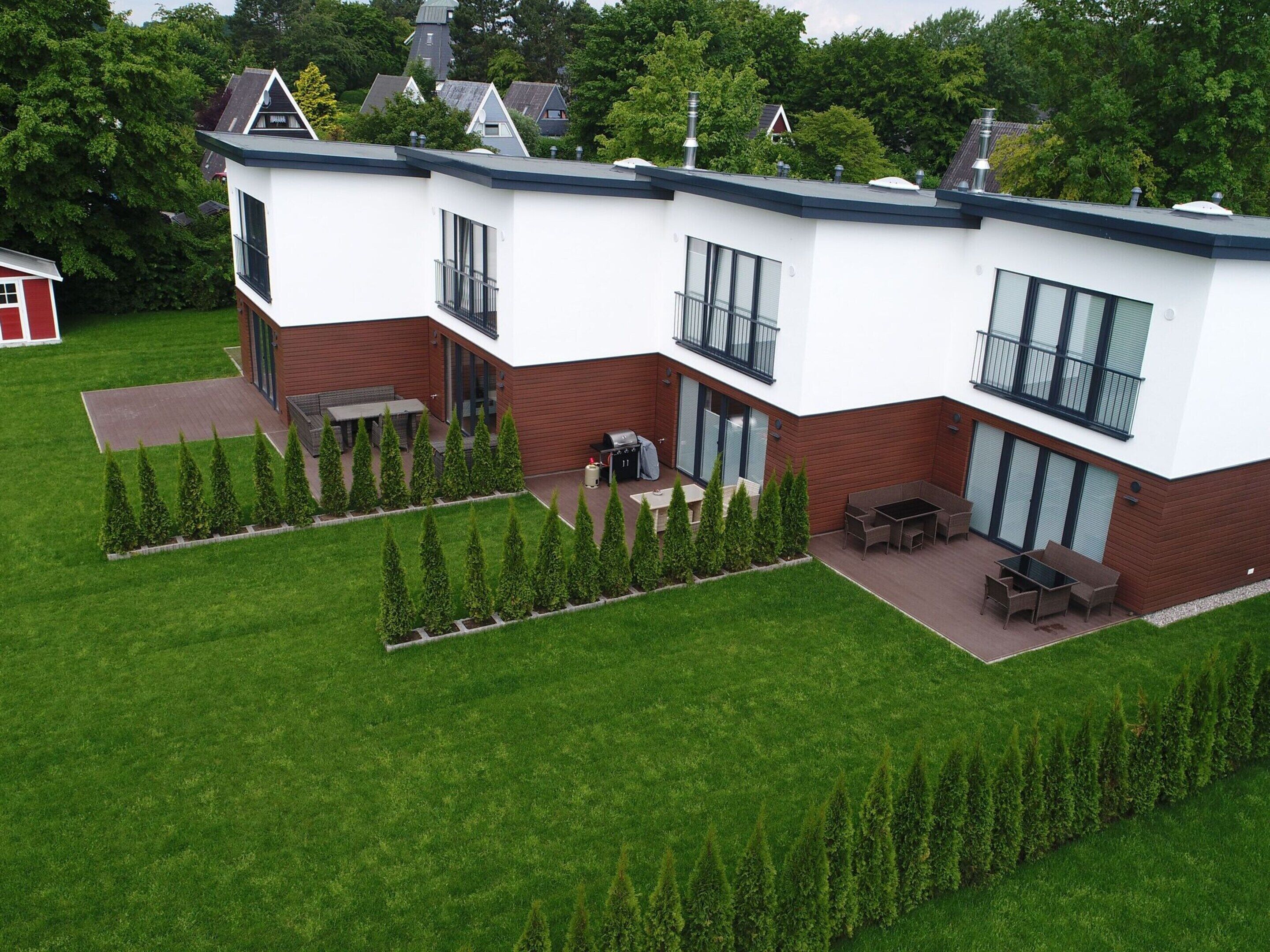 Ein modernes, zweistöckiges Haus mit einer Terrassenanlage, einer Grillgelegenheit und einem kleinen Schuppen im Hintergrund.