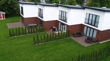 Ein modernes, zweistöckiges Haus mit einer Terrassenanlage, einer Grillgelegenheit und einem kleinen Schuppen im Hintergrund.