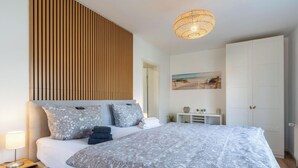 A bedroom with a bed, bedside table, lamp, and a wall-mounted shelf with decorative items. - Ferienwohnung in St. Peter-ording (St. Peter-Ording)