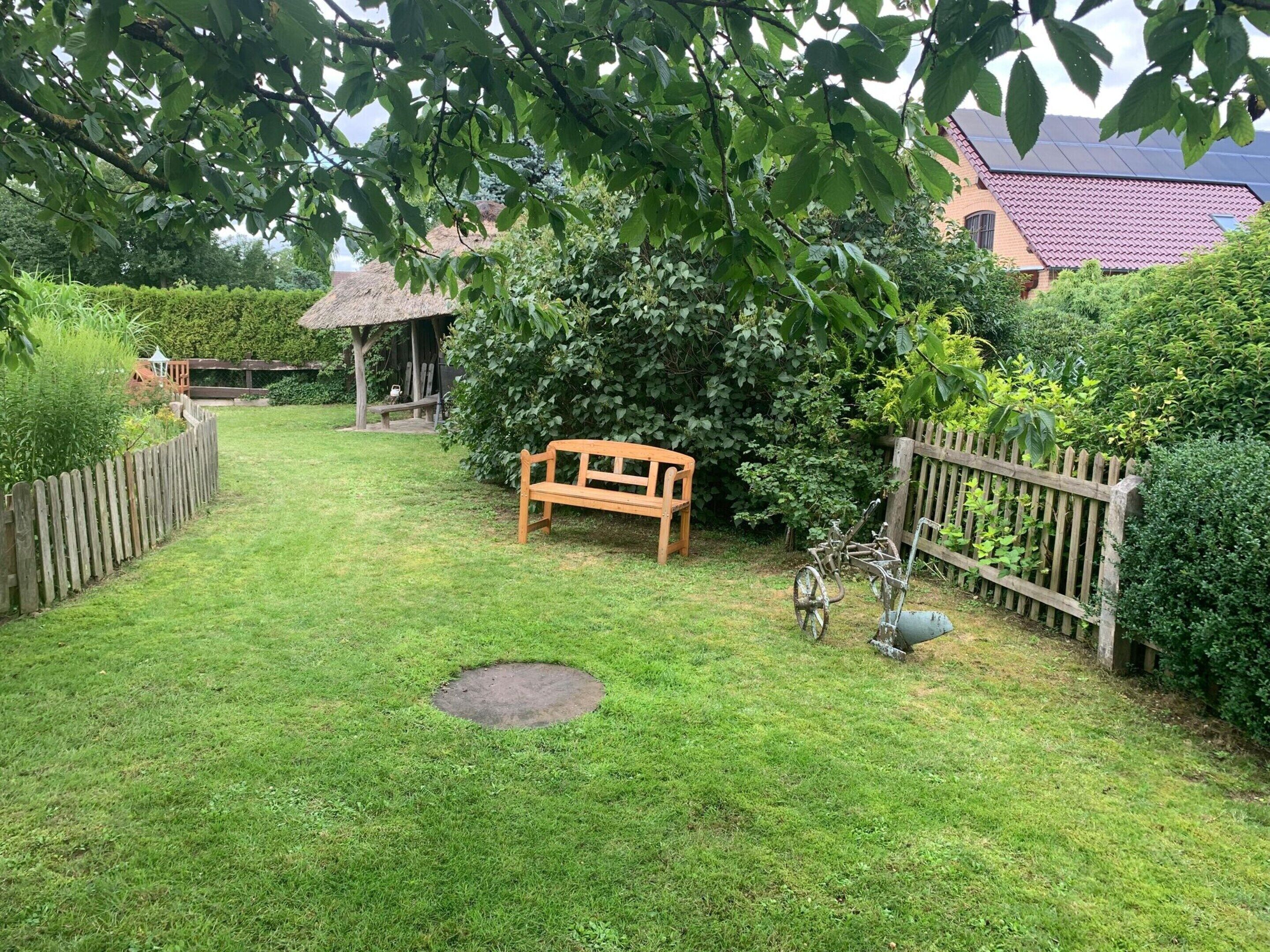 Ein gepflegter Garten mit einer Holzbank, einem strohgedeckten Gebäude und einem umzäunten Bereich.